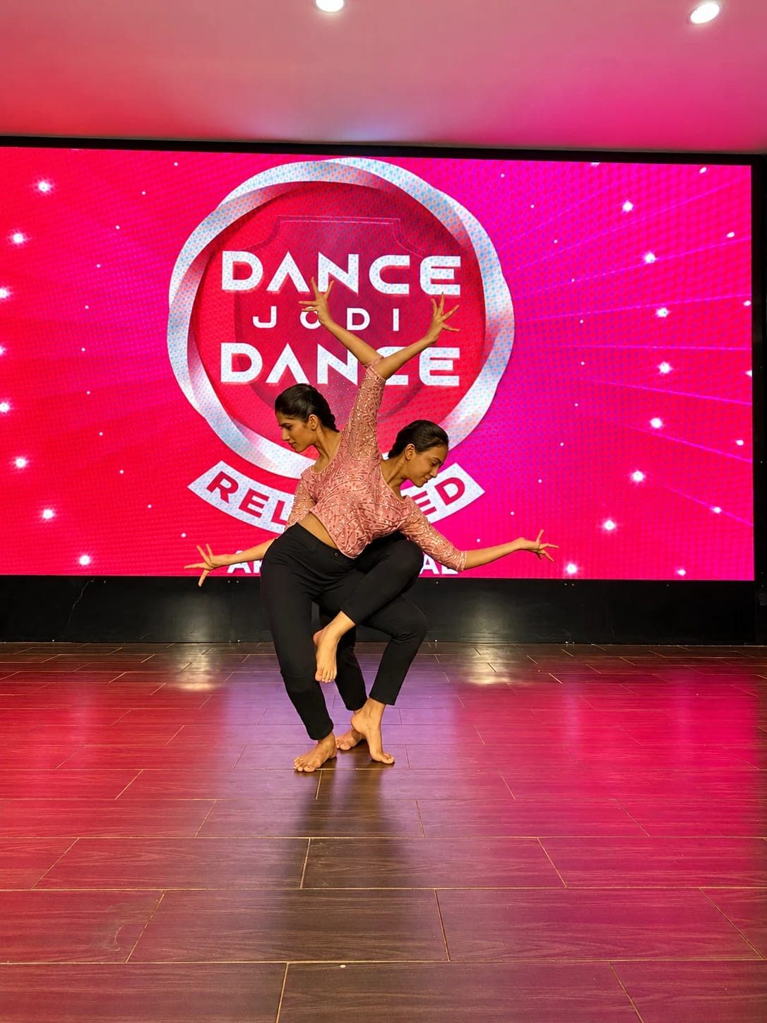 Two dancers in matching pink tops holding a mirrored pose on the Dance Jodi Dance stage