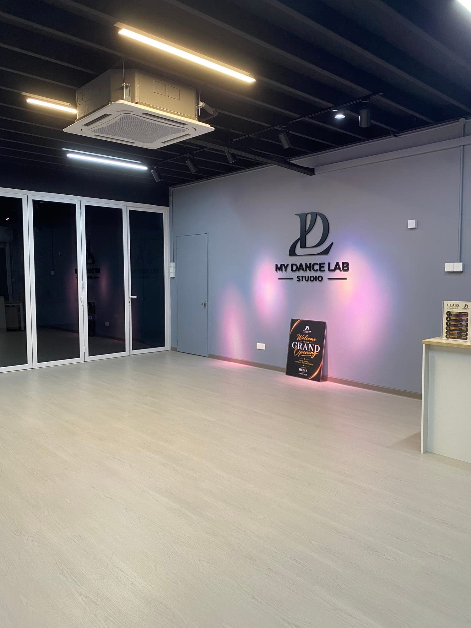 The front of the studio: glass folding doors, the logo wall lit in soft pink, and a grand opening sign