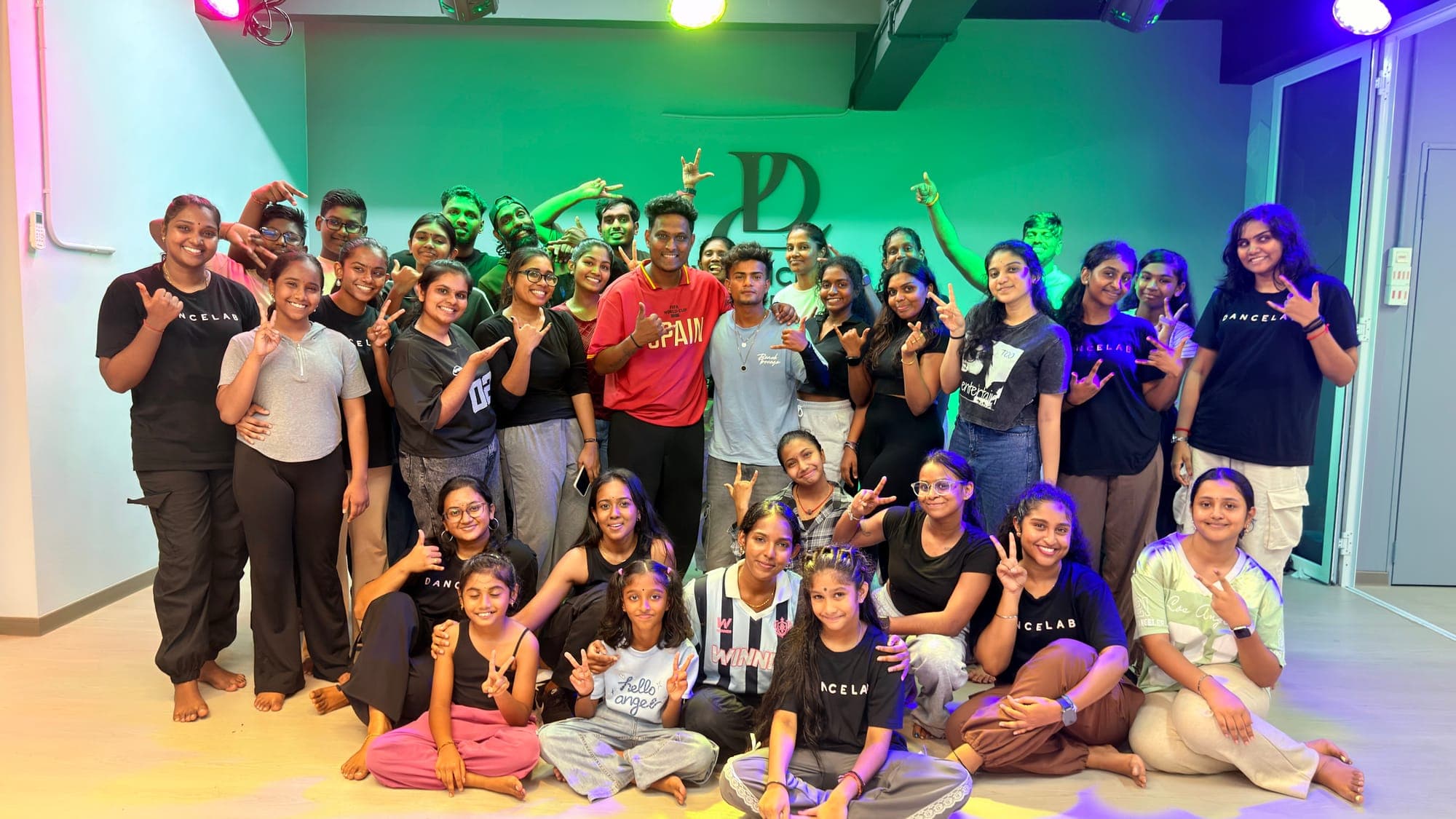 A large group of dancers posing in the studio under green stage lights at the Varadha Master workshop